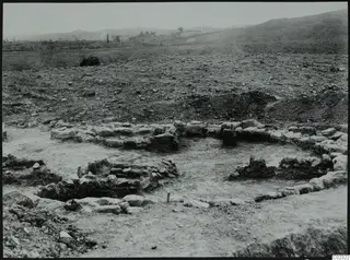 Excavated stone wall foundations at Kythrea, with a rocky hillside and hills behind.