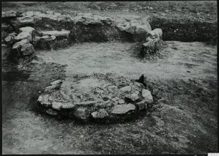 Excavation at Kythrea showing a low circular stone structure in the foreground and stone walls behind it