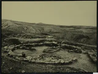 Excavated stone foundations of rounded structures at Kythrea, with bare hills rising behind.