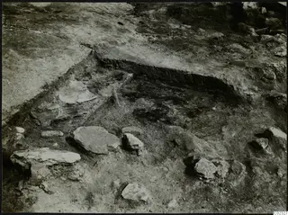 Excavation trench at Kythrea with scattered stones and a pale curved fragment on the trench floor