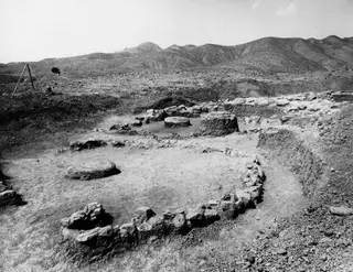 House V at Kythrea after the floor was removed, showing curved stone walls and round stone bases in an excavated area