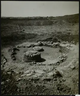 Excavated circular stone foundations at Kythrea, with two rounded stone blocks inside and hills behind.