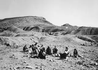 Group of people seated on a stony hillside at Kythrea, with sheep grazing to the right