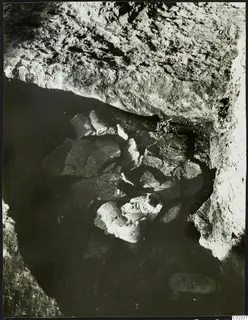 Excavation at Kythrea showing broken objects lying in a rock-cut hollow beneath an overhanging rock face.