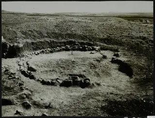 Excavated stone foundations of a round structure in open dry ground at Kythrea
