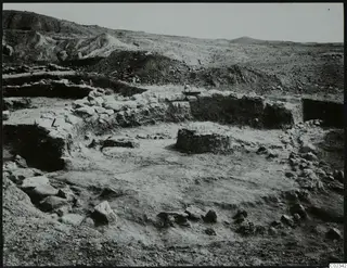 Excavated stone walls and foundations at Kythrea, with spoil heaps and hills in the background.