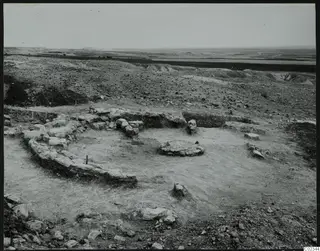 Excavation at Kythrea showing a curved stone wall around a low circular stone base on bare excavated ground