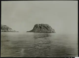 Rocky islet rising from calm sea at Petra tou Limniti, with a second rocky headland at left.