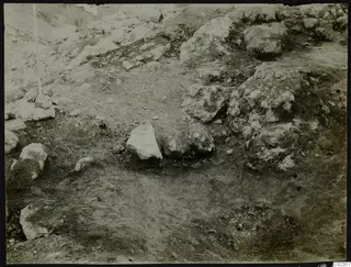 Excavation at Petra tou Limniti showing stones in packed soil, with a stick standing at the left edge.