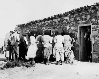 Payment at Vouni: women and men gathered outside a stone building with a wooden doorway.