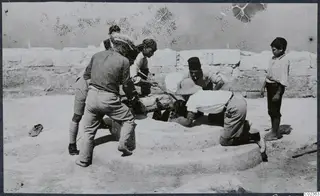 Men and a boy working around a round stone block with a wall of large stone blocks behind them, at Vouni.