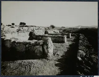Excavated stone walls and foundations of the palace at Vouni, with a stone-lined passage and open hills behind.