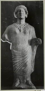 Limestone statue of a standing female figure from Vouni, shown frontal against a dark background.