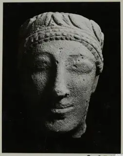 Limestone head from Kition with a carved headband and leaf pattern, photographed against a dark background.