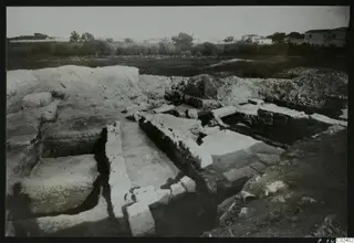 Excavated stone walls and foundations at Bamboula, with houses in the background
