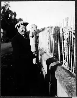 Toulis Souidos smiling, holding a male terracotta sculpture from Ayia Irini beside a wall and iron railing