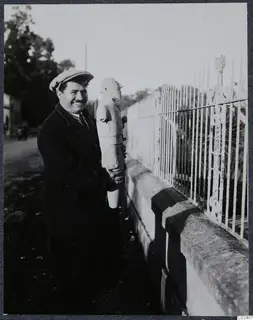 Toulis Souidos smiling and holding a male terracotta sculpture from Ayia Irini beside an iron railing fence