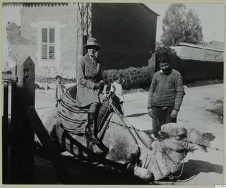 Vivi Gjerstad riding a camel in Nicosia, with a man in a fez and two children nearby.