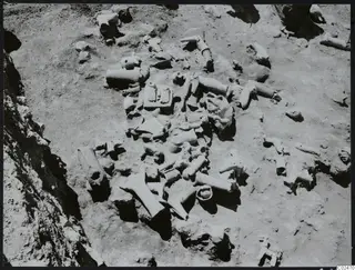In situ finds at Ayia Irini: many pale fragmentary objects lying among stones and soil in an excavated area
