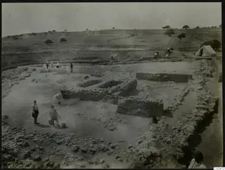 Excavation at Ayia Irini with low stone walls, people carrying buckets across the dug area and a white tent on the right
