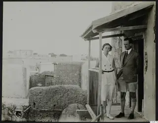 Einar and Vivi Gjerstad standing on a wooden veranda beside a stone and mud-brick building at Ayia Irini