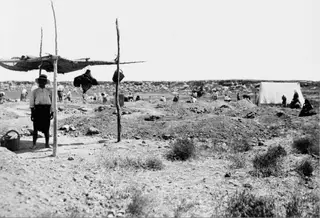 Excavation at Enkomi with spoil heaps, scattered workers and a white tent at the right edge