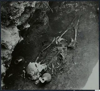Skeleton and two small vessels lying in excavated soil beside a rock face at Enkomi