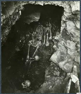 Tomb 14 at Enkomi: skeleton lying in a rock-cut tomb chamber during excavation, with a jug beside it.