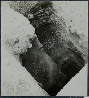 Excavated tomb entrance at Enkomi, with a stone-built wall above a sloping passage leading down to a dark opening