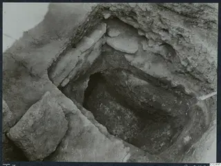Tomb 7 at Enkomi during excavation, showing the tomb chamber cut into soil with large stones.
