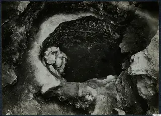 Excavation at Enkomi, looking down into a round cut in rock with a cluster of stones against its rim