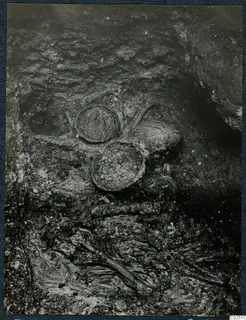 Tomb 14 at Enkomi during excavation, with round vessels and skeletal remains in dark soil