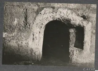 Built tomb chamber seen through a plastered arched doorway, with a recess beside it holding an upright object