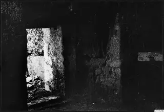 Interior of a built tomb chamber with large stone blocks around a doorway opening, rubble at the lower left