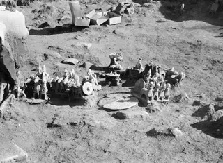 Terracotta carts and small clay figures lying in a cluster on excavated ground at Ayia Irini