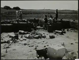 In situ broken pottery in an excavation trench at Ayia Irini, with workers standing and sitting along the trench edges.