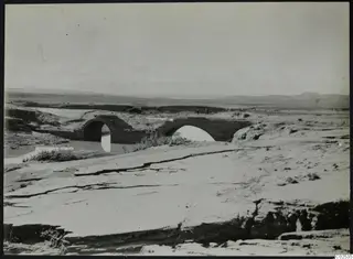 Stone arched bridge over a stream at Ayia Irini, with two small figures on the far bank