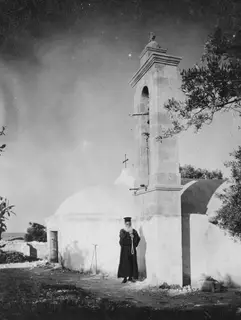 Papa Prokopios holding the bell rope beside the bell tower of the church at Ayia Irini