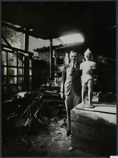 Rubert Gunnis standing beside a sculpture of a standing figure on a wooden crate, in a workshop at Nicosia
