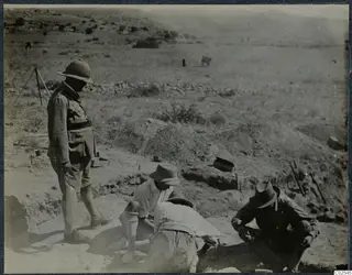 Men digging in a trench at Ayios Iakovos while a man in a pith helmet stands at the edge watching
