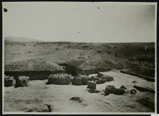 Excavated area at Ayios Iakovos with low stone walls and an earth bank, under a wide open sky.