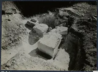 Excavation at Marion, T.86, with large pale stone blocks lying in a dug pit and grass along the edges