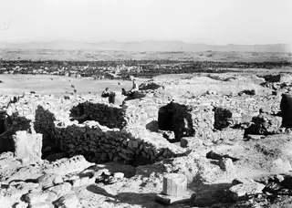Ruined stone walls of the Acropolis at Idalion, with three seated people, a village with trees, and mountains beyond