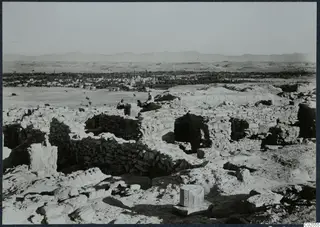 Ruined stone walls of the acropolis at Idalion, with a town, trees and hills in the distance.