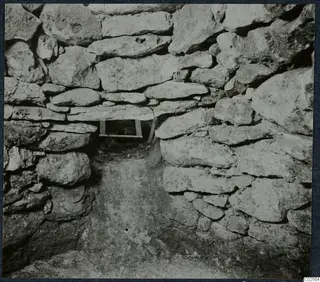 Tomb chamber at Enkomi during excavation, with walls of stacked stones and a wooden frame in the far opening.