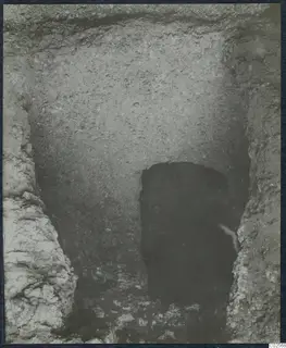 Excavated cutting with rough earth walls leading down to a dark tomb entrance at Enkomi