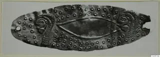 Embossed metal mouthpiece from Enkomi: an elongated oval plate with spiral motifs at each end and small raised rings across its surface.