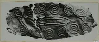 Fragment of thin metal sheet with embossed spirals and a central raised ridge, recorded as a mouthpiece