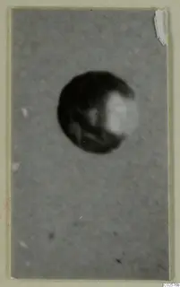 Blurred photograph of a round dark object, a find from Enkomi, shown against a plain grey background
