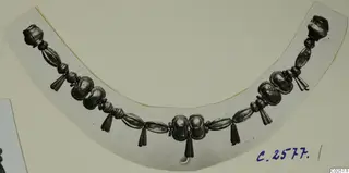 Curved necklace of metal beads with tassel-like pendants, photographed on a pale card.